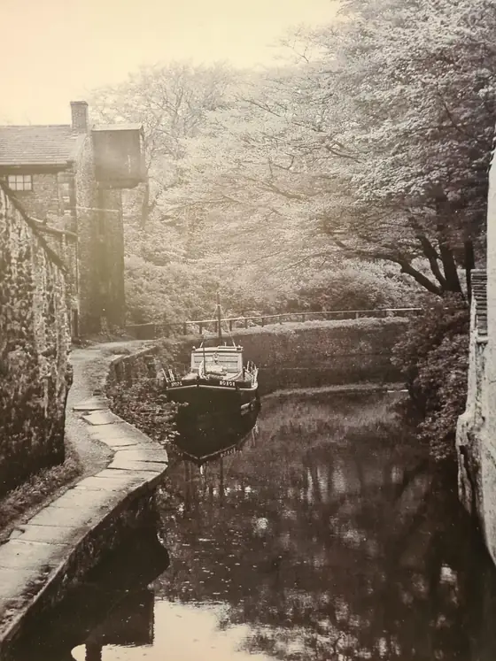 An old sepia photograph of a barge on the canal in a wooded cutting beside the mill