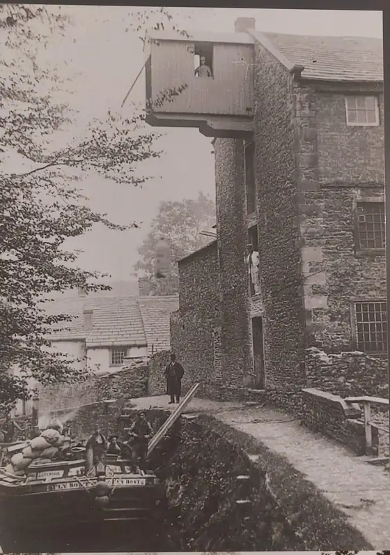 An old black and white photograph of the mill&rsquo;s timber loading bay projecting over the canal, with a loaded barge below