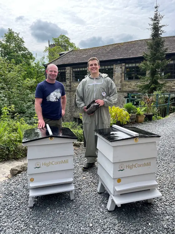 Two beekeepers standing behind the hives with the mill behind them