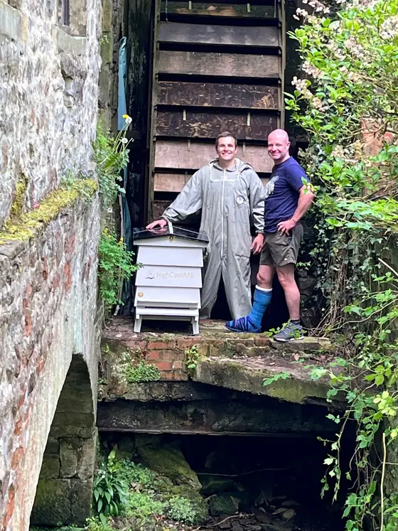 Two beekeepers with a hive in the stone arch beneath the waterwheel