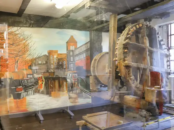 Millstones and wooden gearing in a display case with a painting of the canal behind