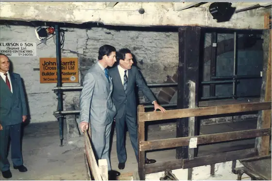 The Prince of Wales beside the waterwheel guard rail, builders’ boards on the wall behind