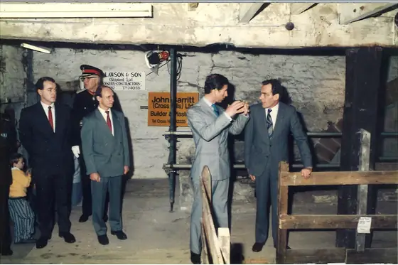A group in suits gathered by the timber guard rail at the waterwheel