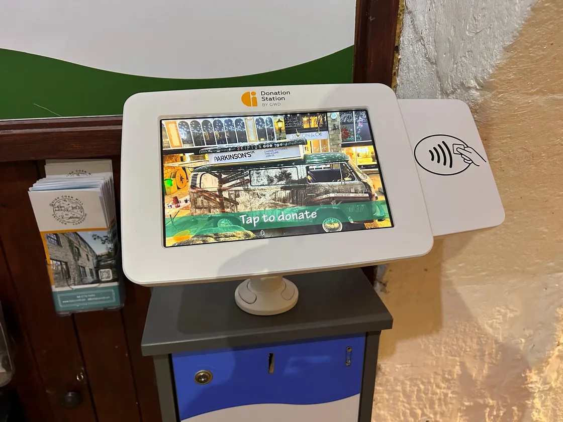 A contactless donation station inside the mill, with Skippy the camper van and &lsquo;Tap to donate&rsquo; on the screen