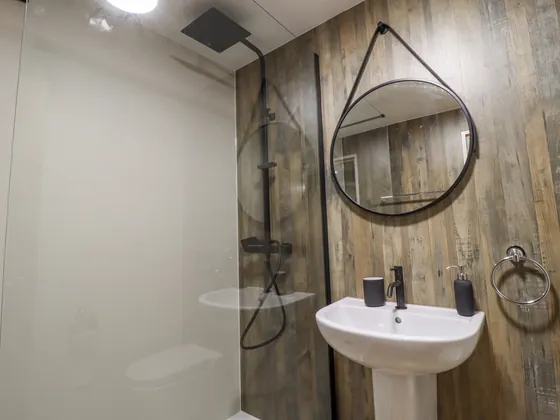 A shower room panelled in wood, with a round mirror over the basin