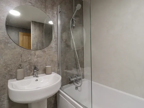 A bathroom with a pedestal basin, a mirror and a bath with a shower over it