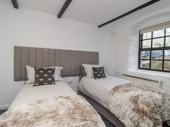 A twin room with bee cushions and fur throws, and a window to one side