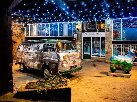 The camper van and a painted sheep sculpture under lights outside the shopfronts